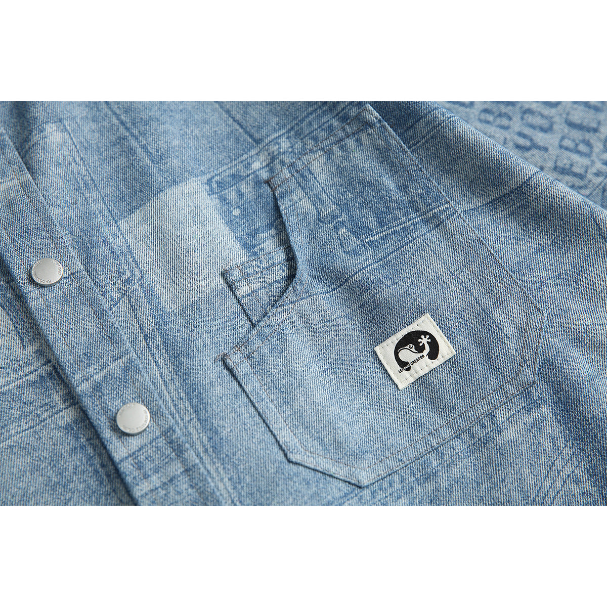 Close-up of the shirt's light blue patterned chest pocket, stitched seams, snap buttons, and sewn emblem patch.