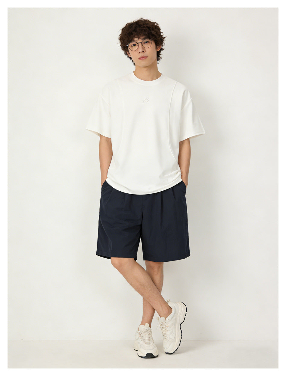 Model wearing a white oversized T-shirt with a small chest emblem and navy shorts, shown from the front.