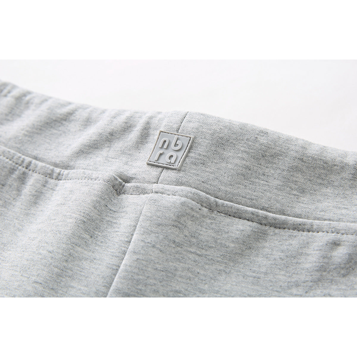 Close-up of the back waistband and small square emblem on light gray shorts.