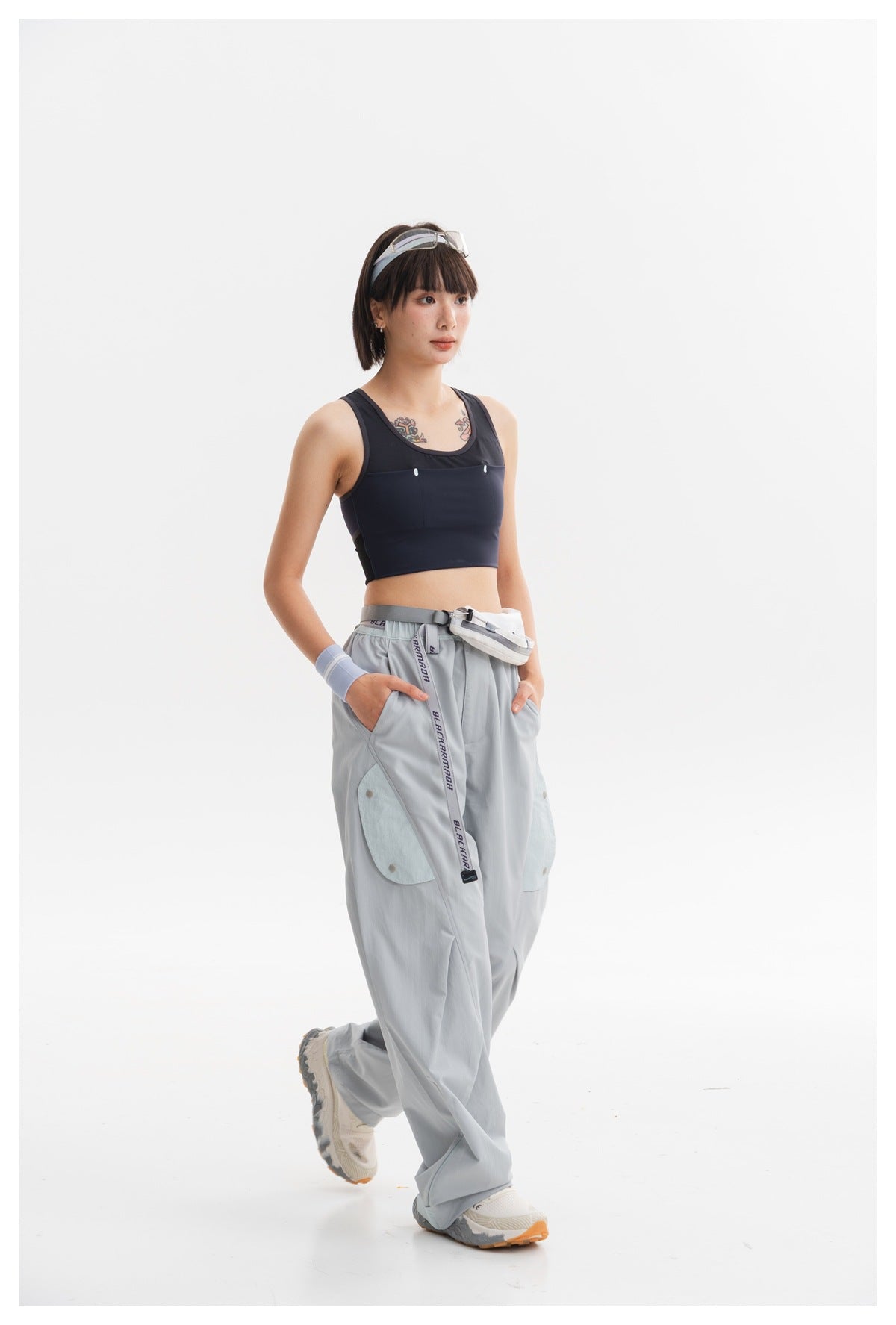Three-quarter view of a model wearing a navy cropped tank and pale blue-gray cargo pants with a white waist pouch.