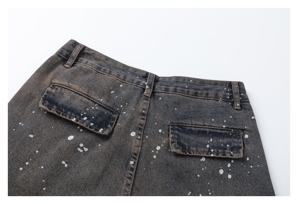 Rear view of dark washed denim trousers with two flap pockets, belt loops, and pale paint splatters.