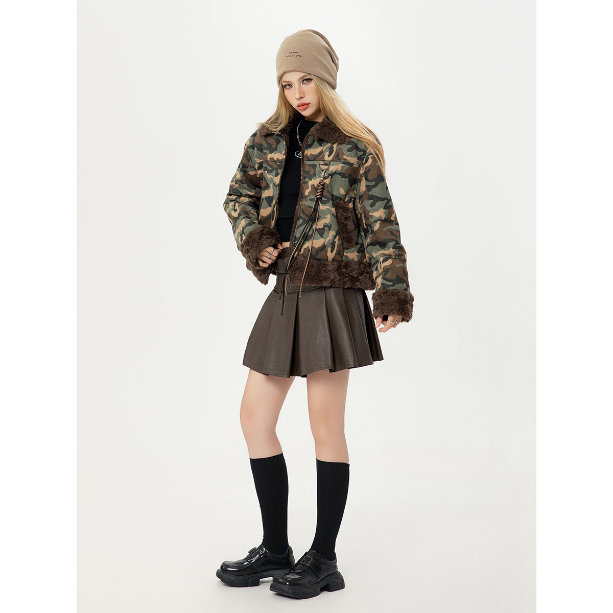Model wearing a brown, olive and tan camouflage jacket with dark brown plush trim, paired with a brown skirt and beige