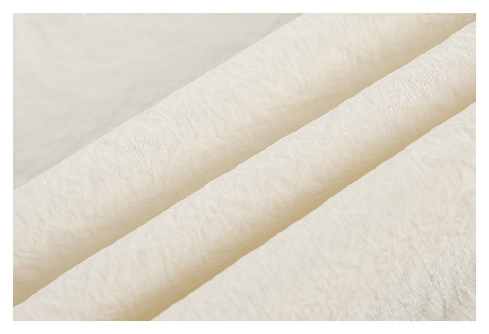 Close-up of cream fabric folded into diagonal ridges, showing its fine textured surface.