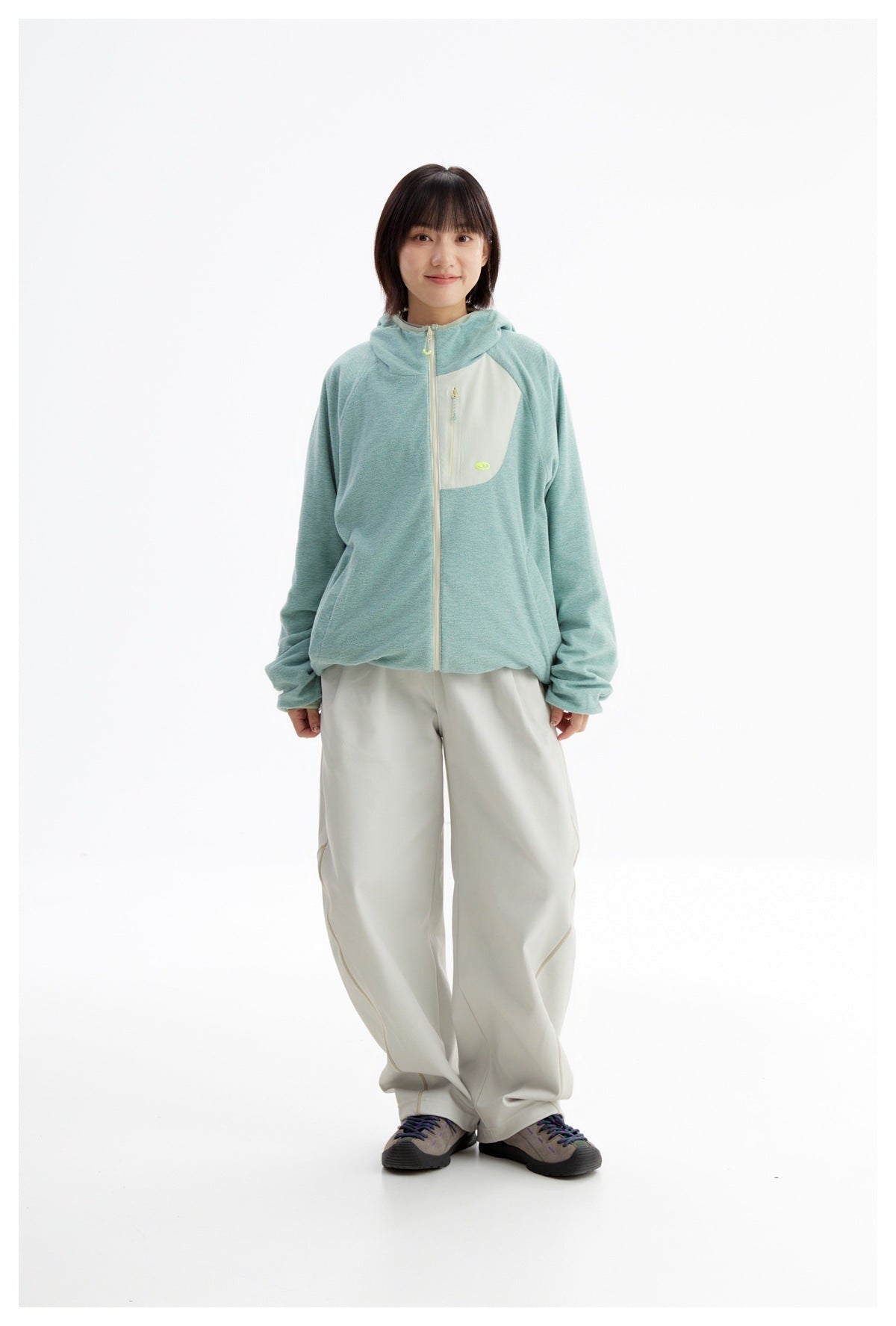 Front view of a model in a mint-green hooded zip jacket with a cream chest panel and ivory pants.