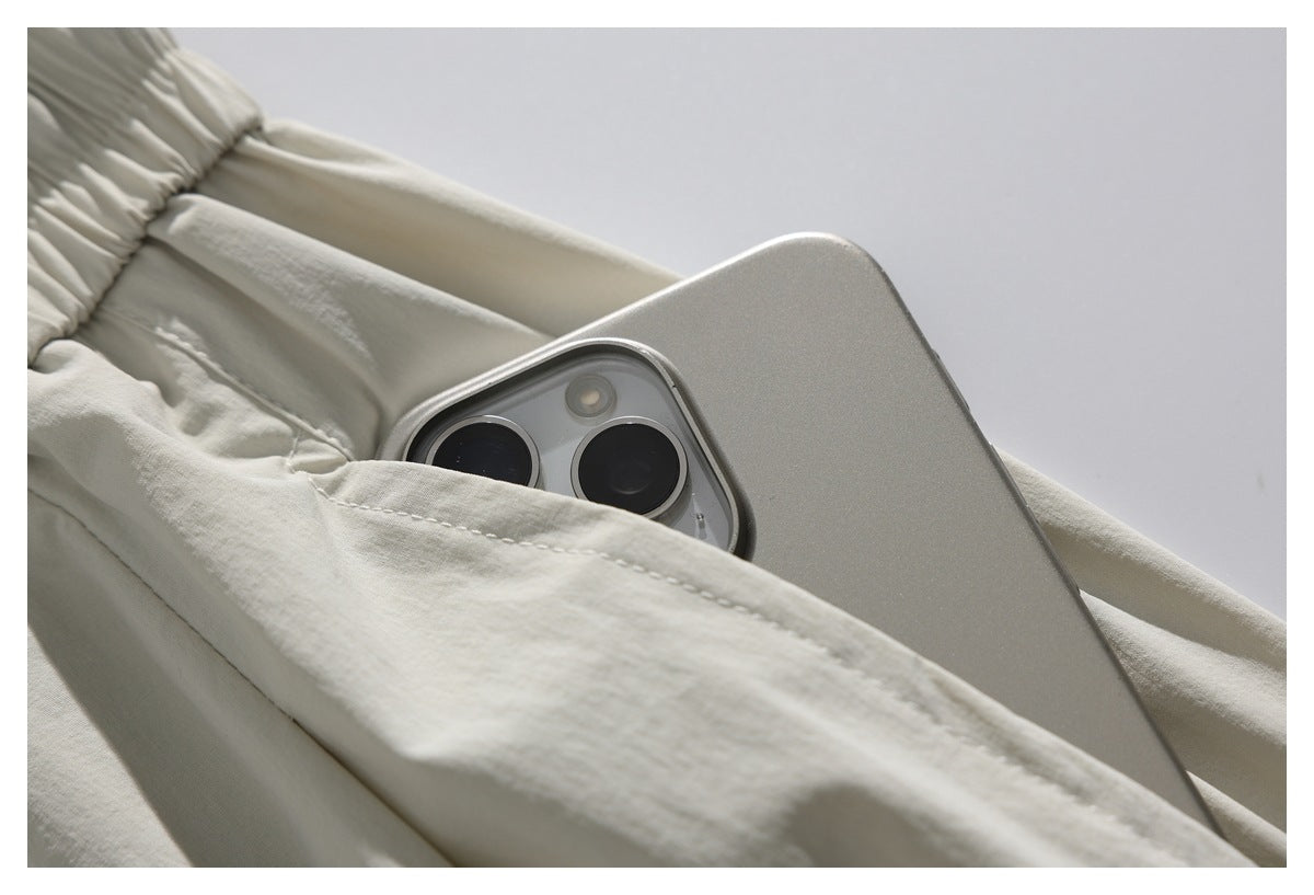 Close-up of an off-white garment pocket holding a silver smartphone, showing the pocket stitching and gathered edge.