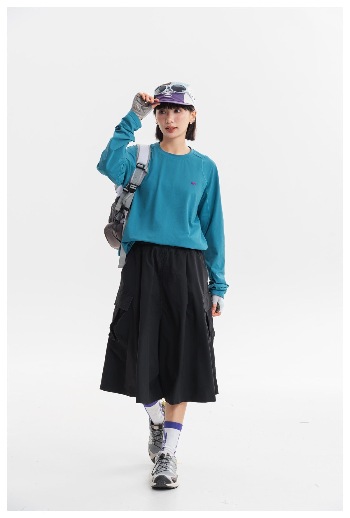 Model wearing a teal long-sleeve top and black cargo midi skirt, walking in a front view.