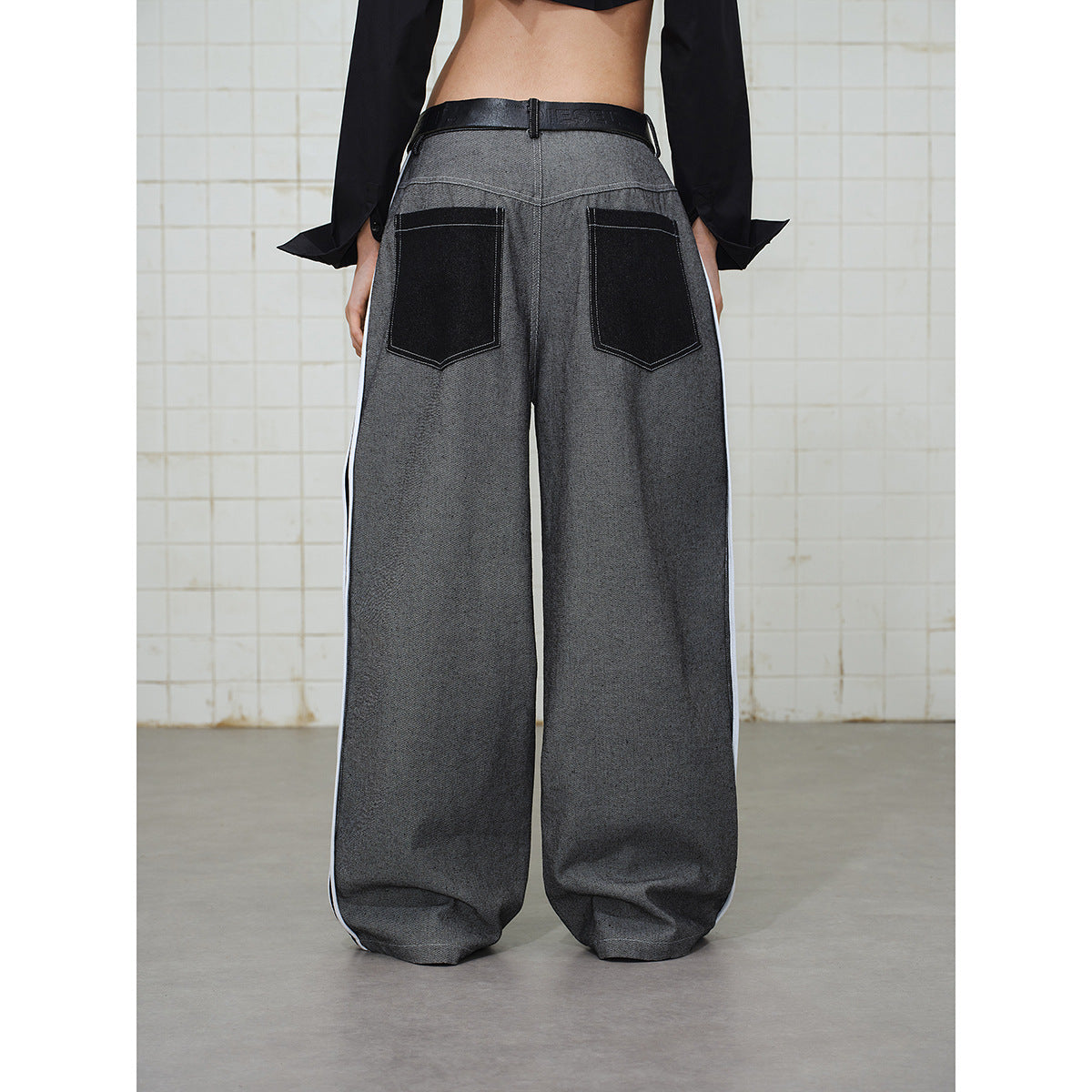 Back view of a model wearing wide gray trousers with black back pockets and white side stripes.