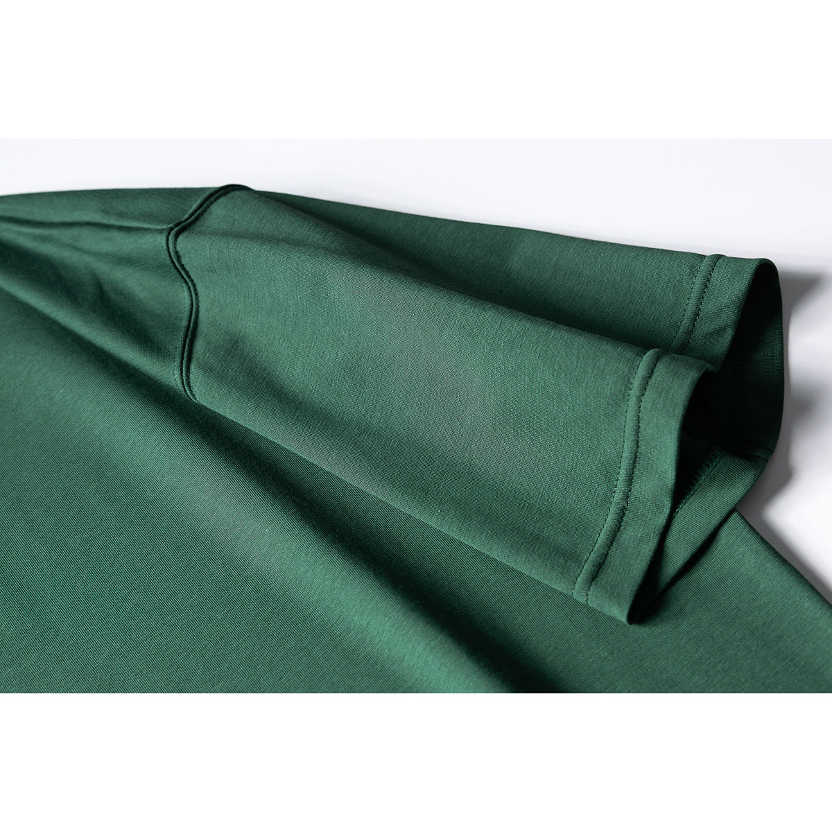 Close-up of a dark green T-shirt sleeve and stitched hem, folded over the shirt body.