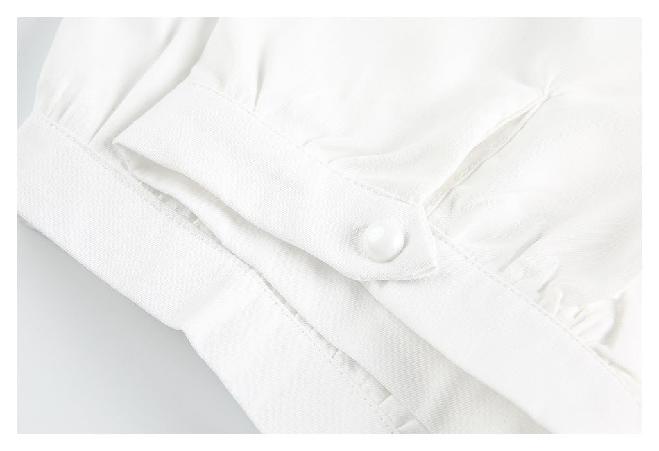 Close-up of a white sleeve cuff with a button and gathered fabric.