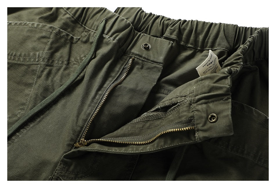 Close-up of olive-green pants with the front fly open, showing a brass-colored zipper and inner waistband.