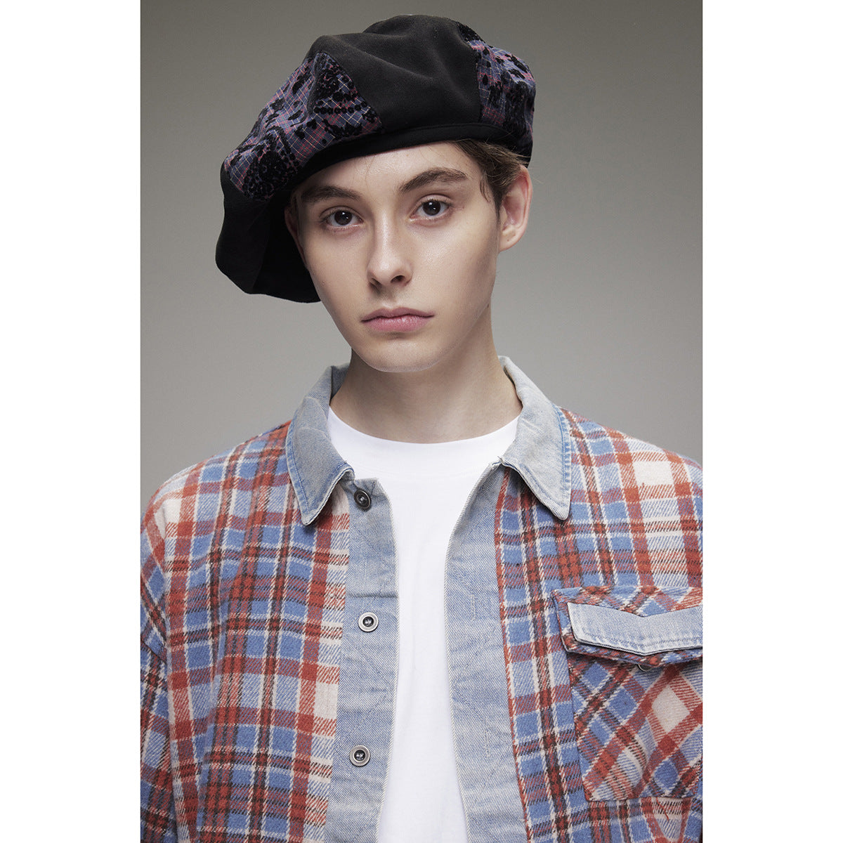 Close-up of a model wearing a blue, rust and cream plaid overshirt with a pale collar, button placket and flap chest pocket.