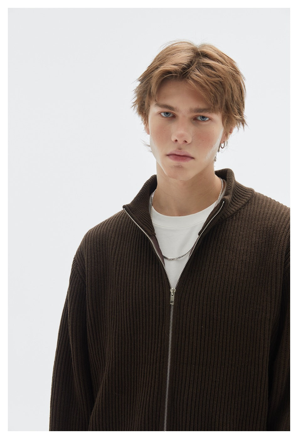 Close view of a model wearing a dark brown ribbed zip cardigan open over a white shirt.