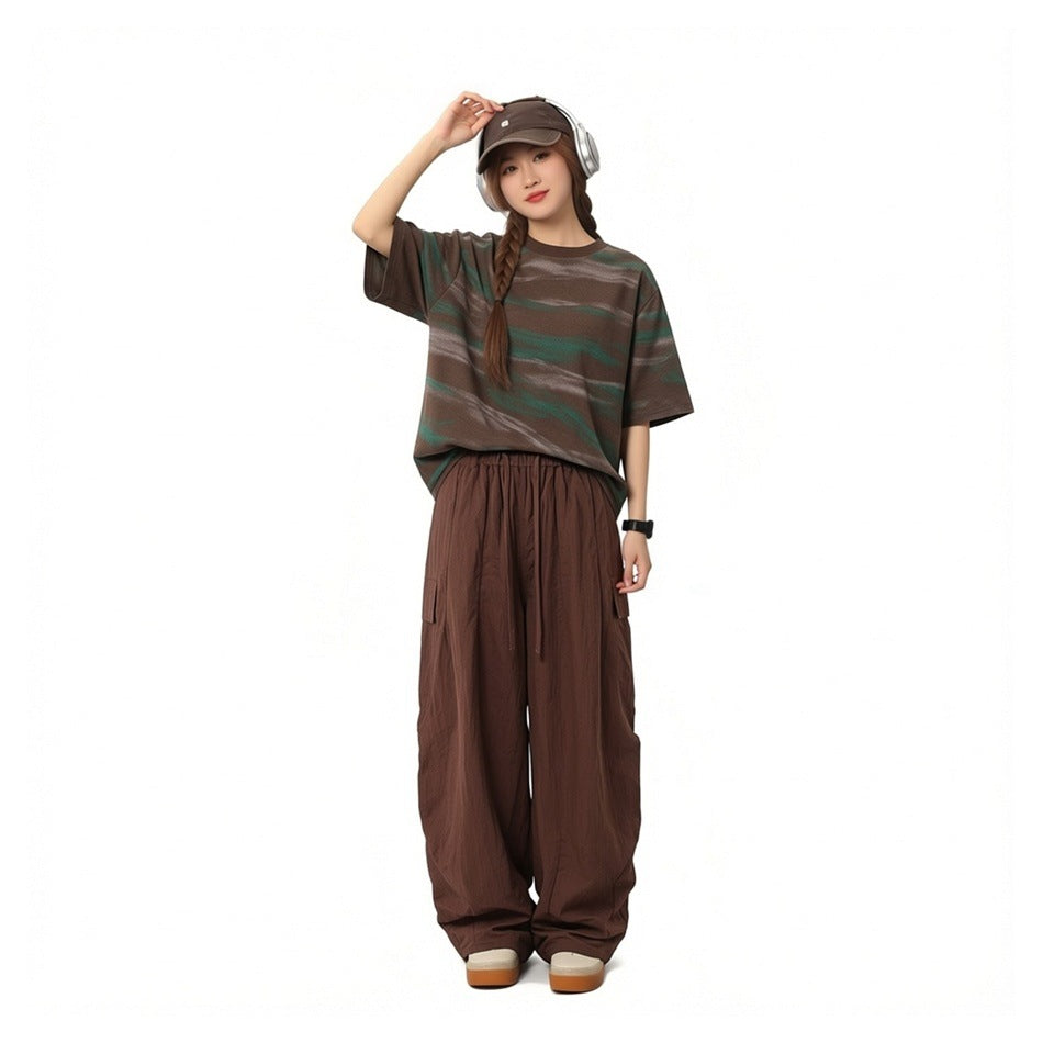 Person wearing brown wide-leg cargo pants with a striped short-sleeve tee, cap and headphones