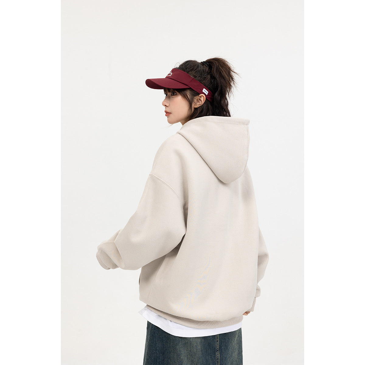 Rear view of a model wearing an oversized cream hoodie with the hood down over the back.