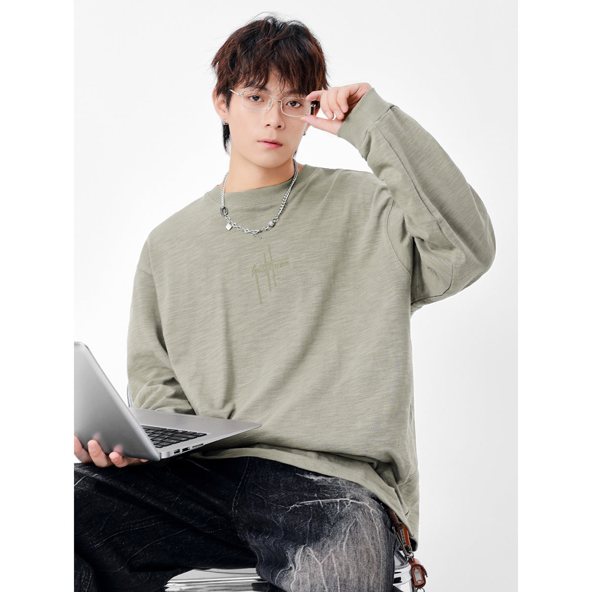 Model wearing an oversized muted sage long-sleeve shirt with a subtle chest graphic.