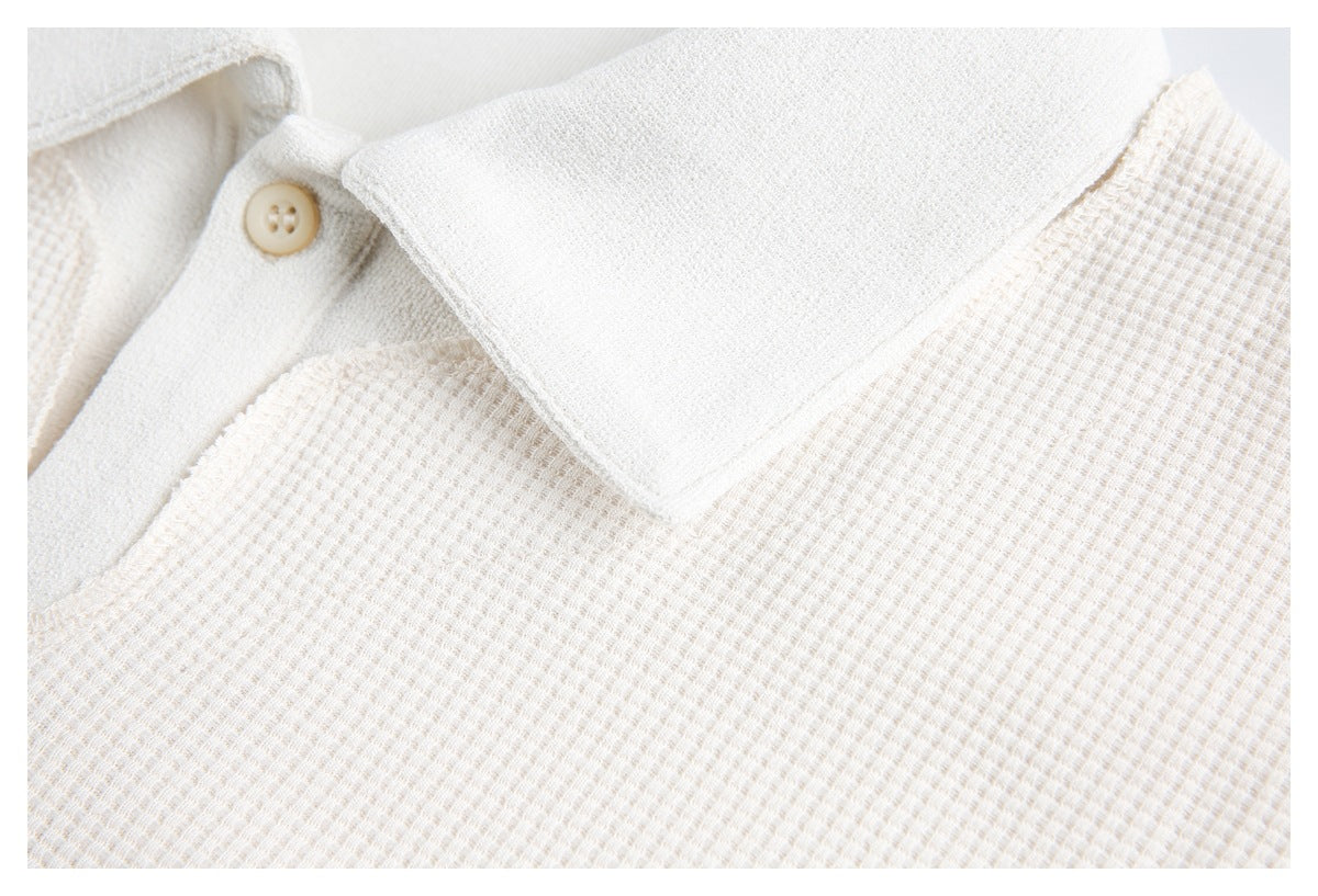 Close-up of an off-white polo's broad collar, beige button, and textured waffle-knit body.