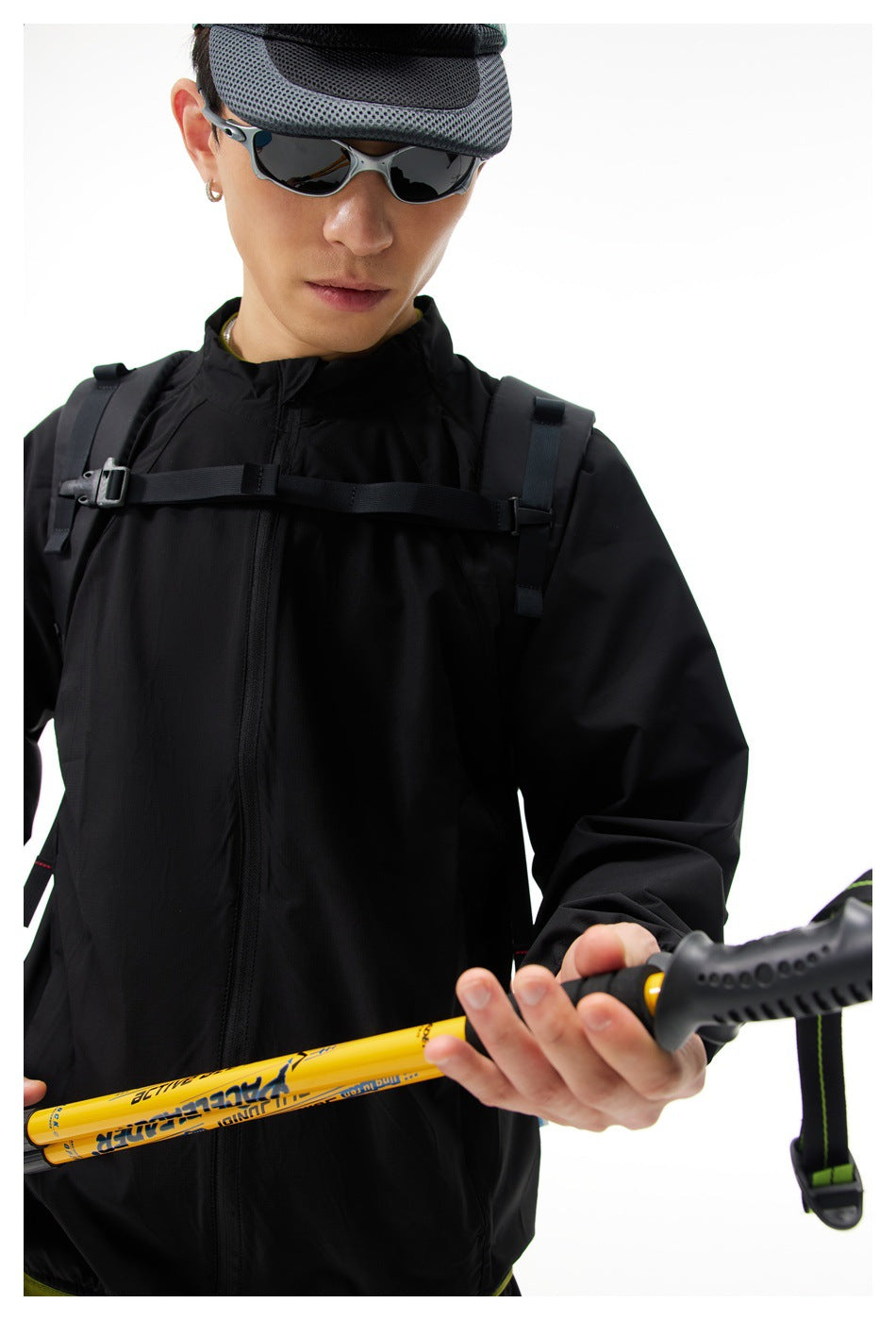Close view of a black zip-front hiking jacket worn with backpack straps and trekking poles.
