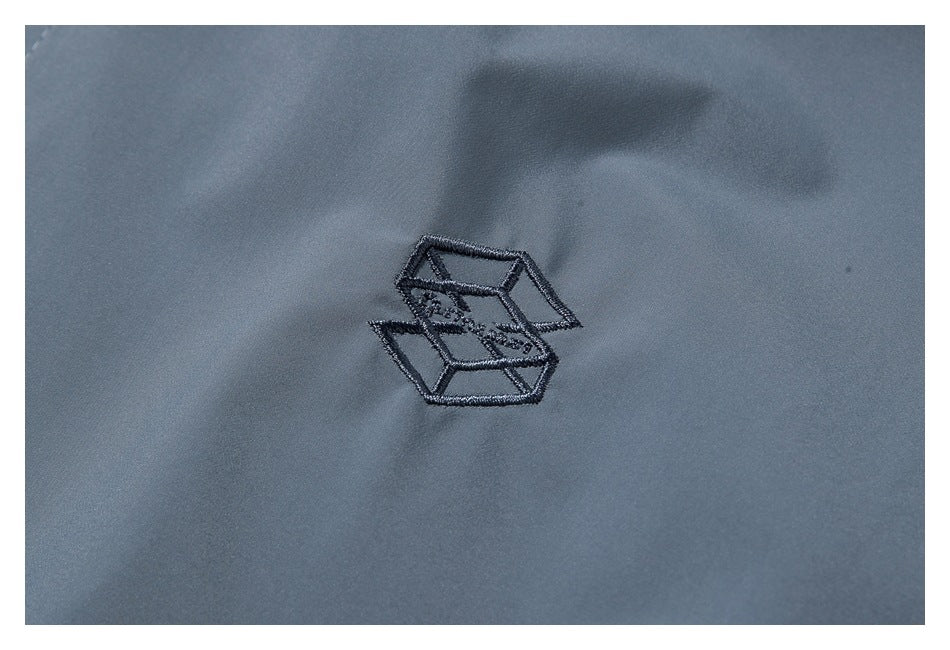 Small dark geometric embroidered emblem on gray-blue garment fabric.