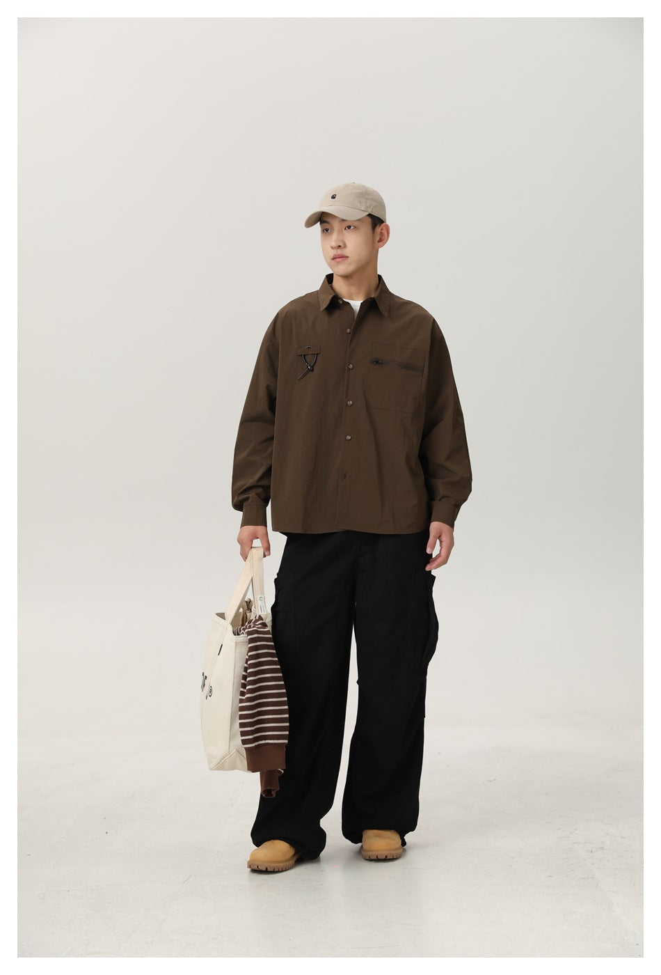 Full-length model wearing a dark brown button-front shirt with black cargo pants and carrying a canvas tote.