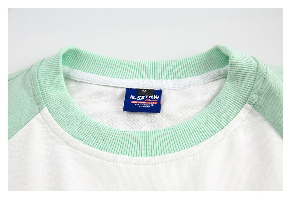 Close-up of a mint ribbed crew neckline on a white raglan shirt, with a sewn neck label.