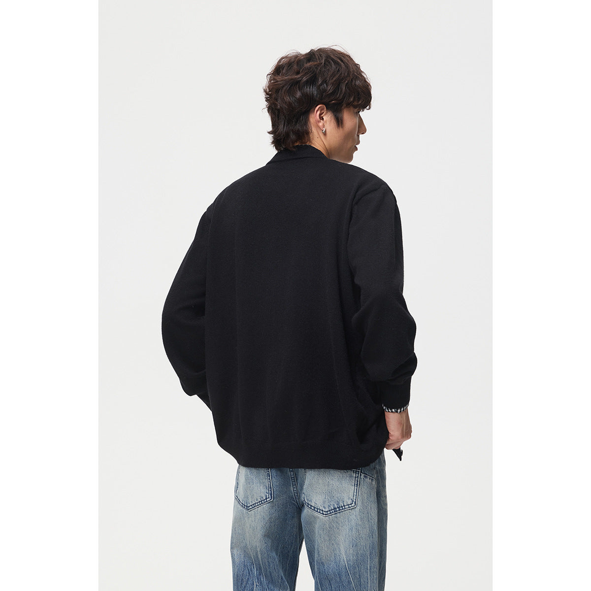 Back view of a model wearing a plain black cardigan with blue jeans.