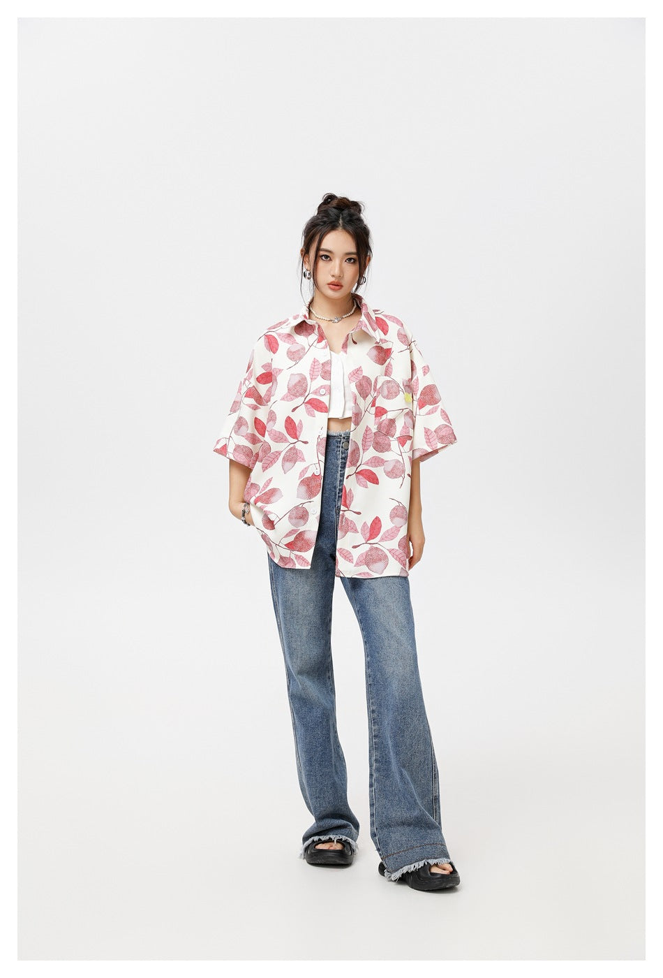 Model wearing an oversized pink leaf-print short-sleeve shirt open over a white top with wide-leg jeans