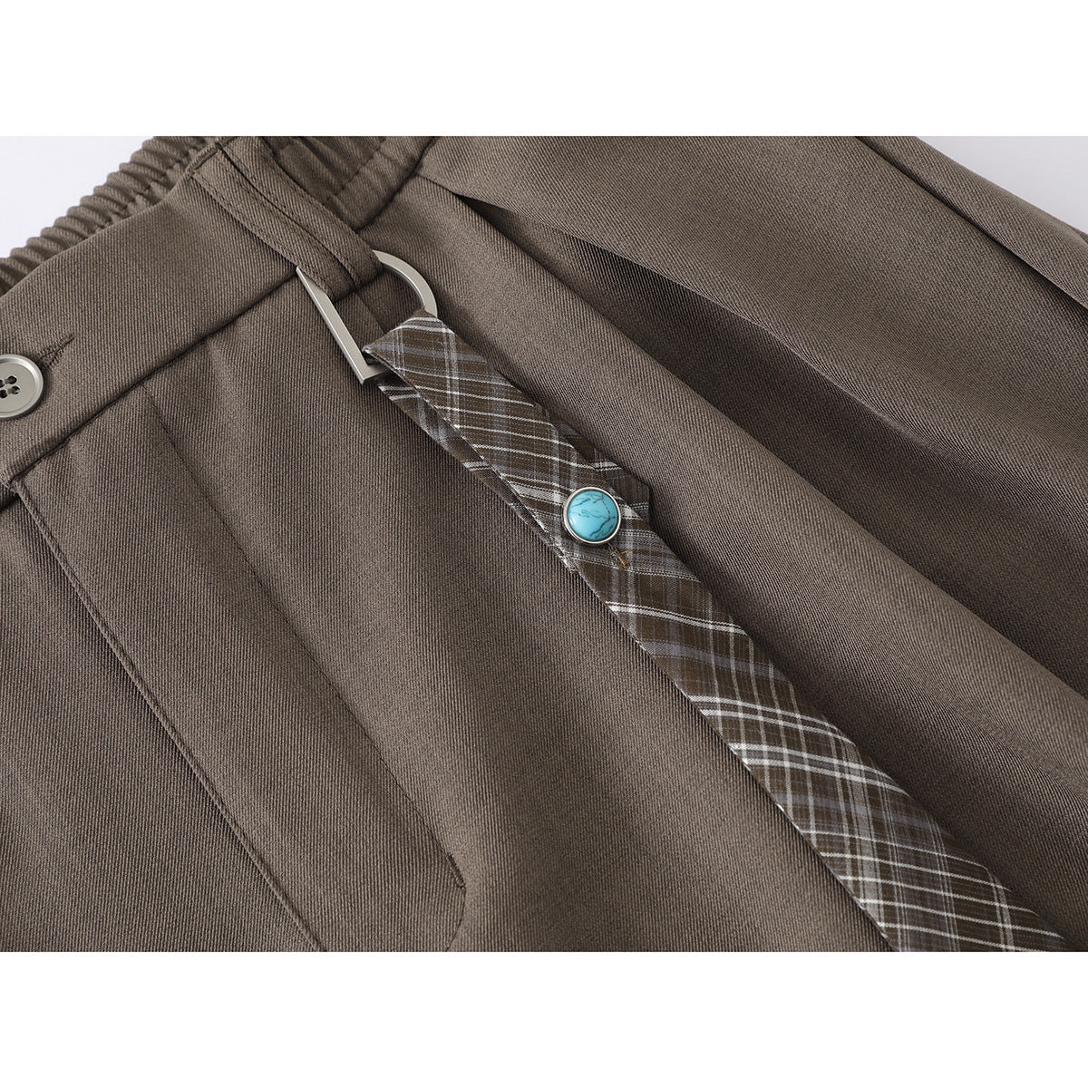 Close-up of taupe shorts with a plaid hanging strap, metal loop, and round turquoise accent.