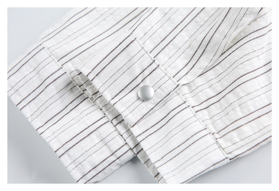 Close-up of a white button on a cuff with fine dark stripes and stitched edges.