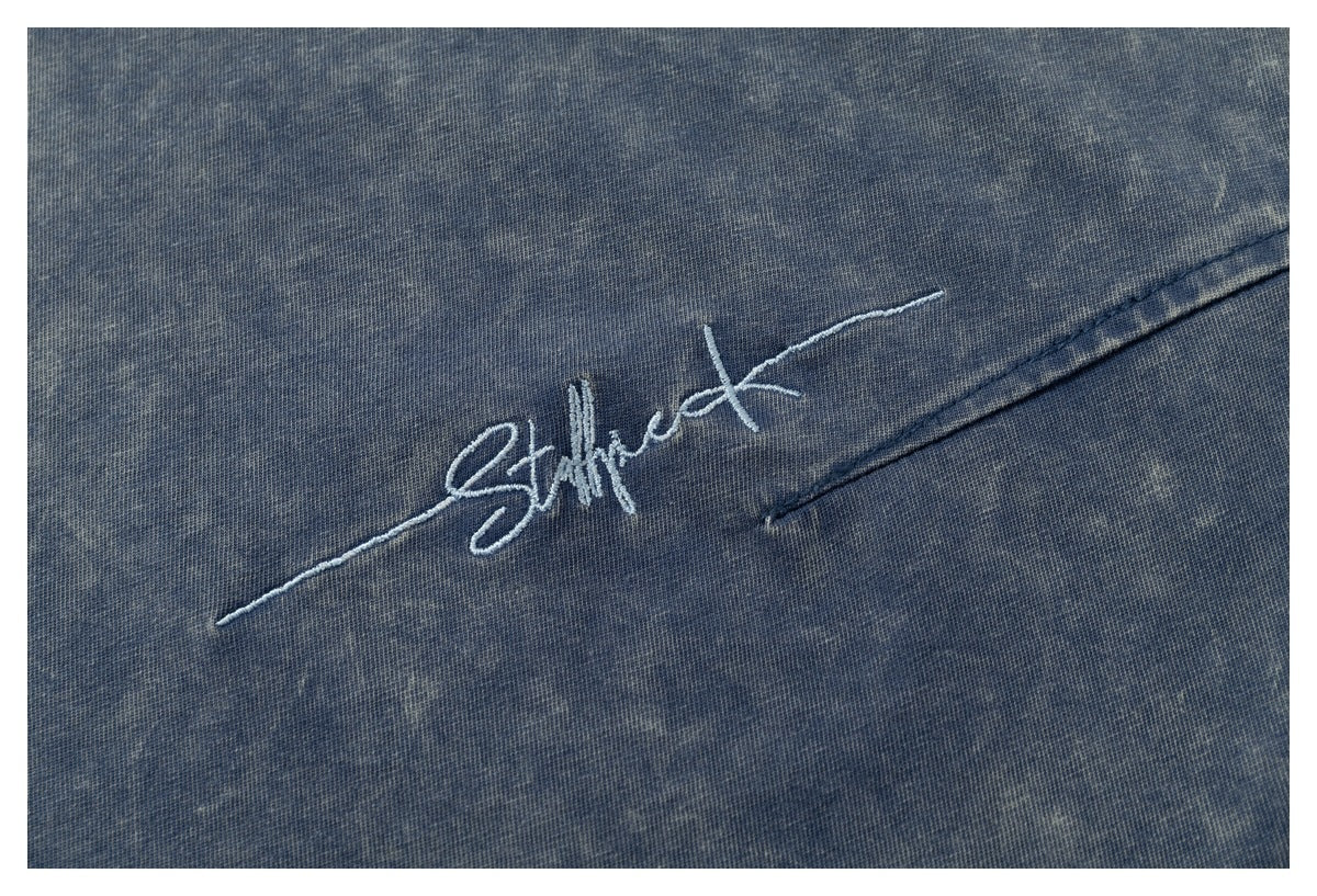 White script embroidery and a seam on mottled blue acid-wash fabric.