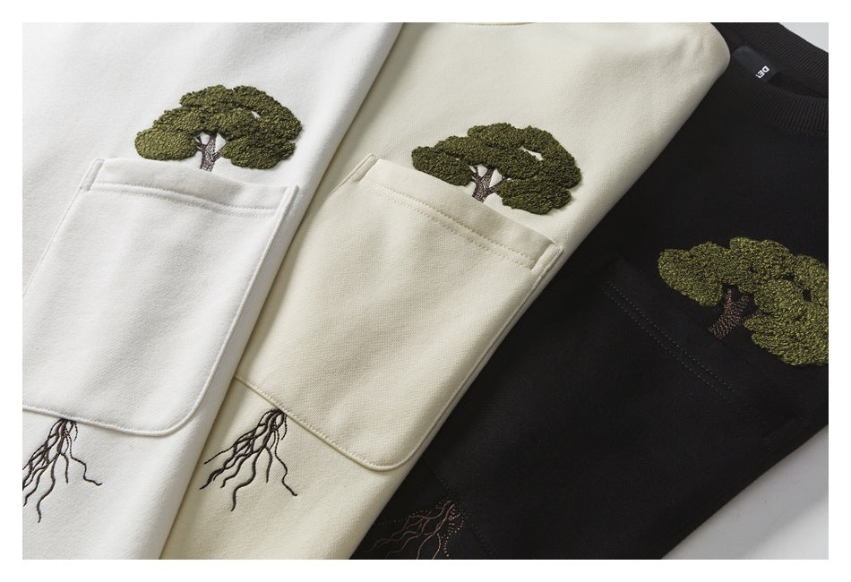 Close view of white, cream, and black sweatshirts with chest pockets and embroidered tree designs.