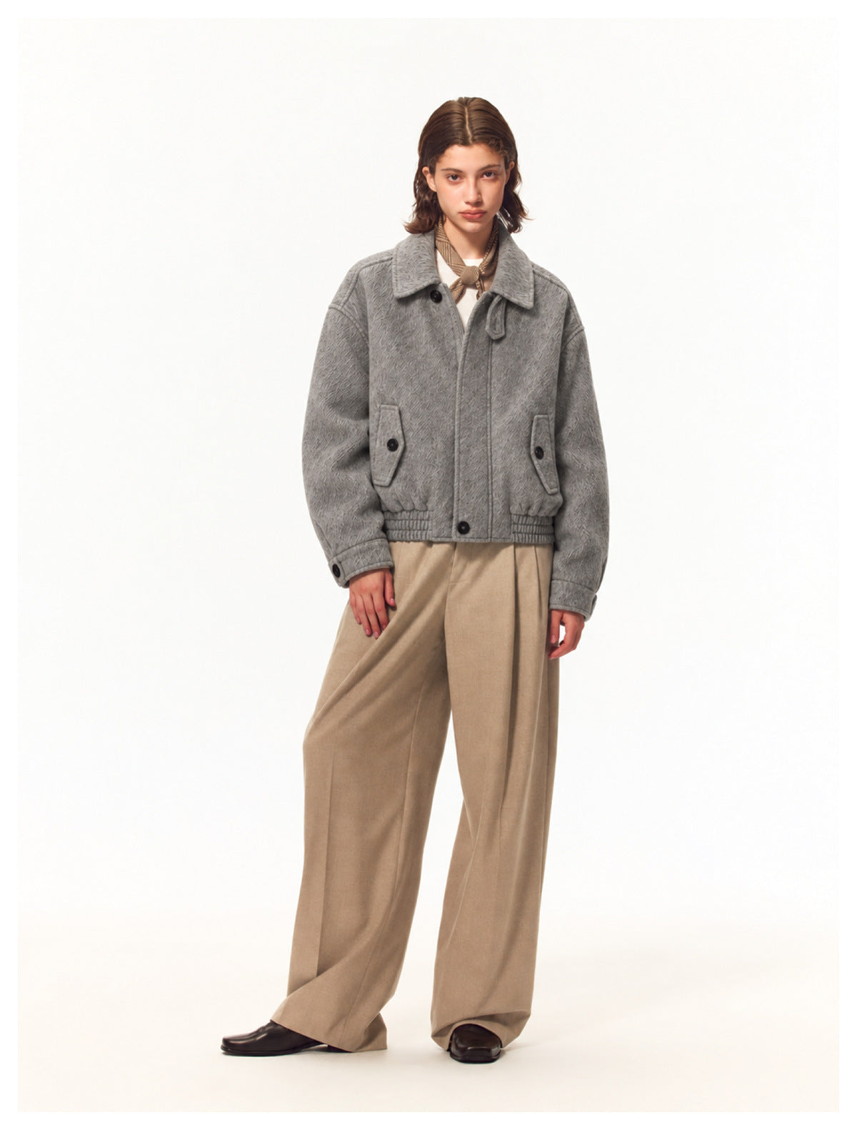Full-length model wearing a gray textured jacket with buttoned pockets, paired with beige trousers.