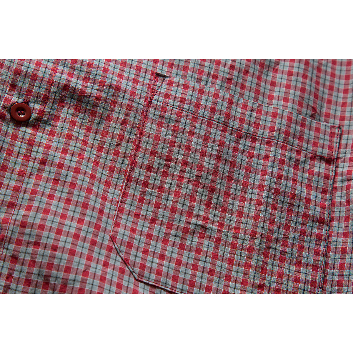 Close-up of the chest pocket and button on a red, gray, and blue plaid shirt.