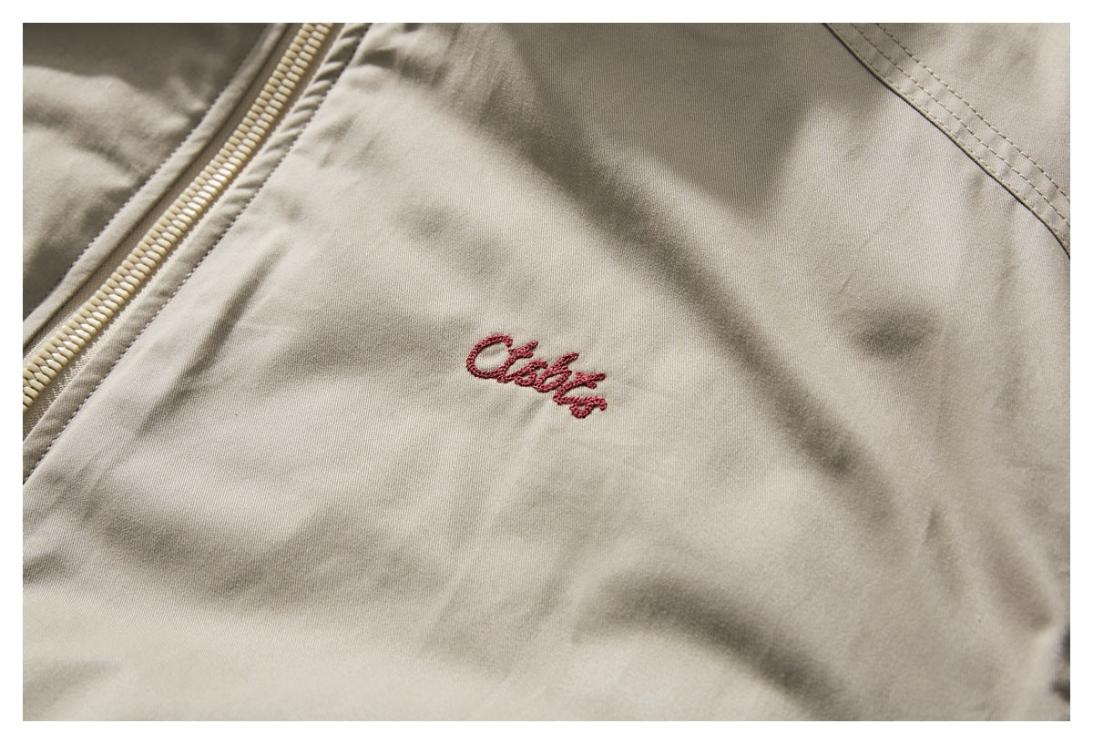 Close-up of red cursive embroidery on the chest of a beige jacket.