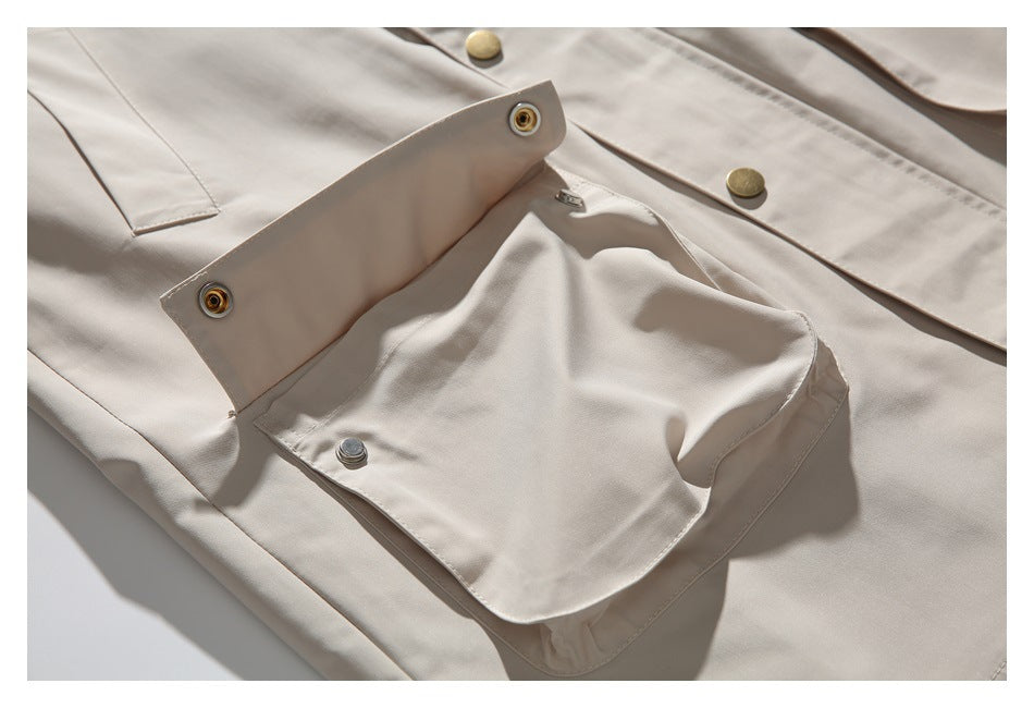 Close-up of a light beige jacket's flap pocket, snap fasteners, and brass-tone front buttons.