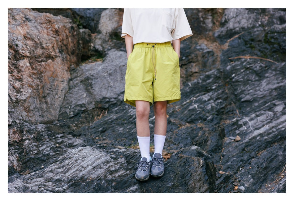 Model wearing bright yellow-green drawstring shorts with side pockets, shown from the front outdoors.