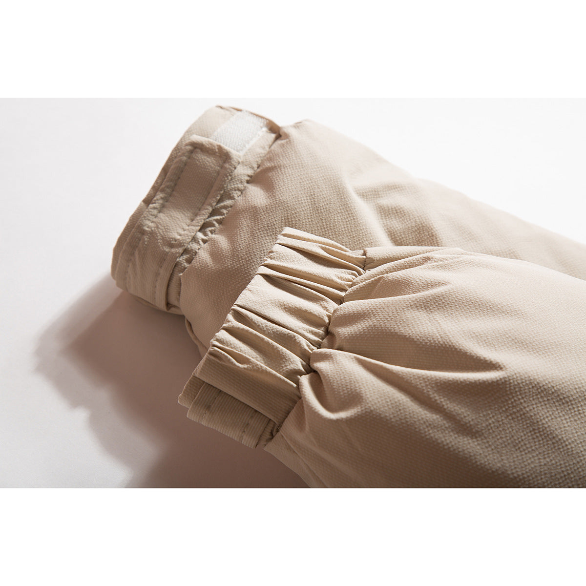 Close-up of a beige jacket sleeve with a gathered cuff and adjustable tab.