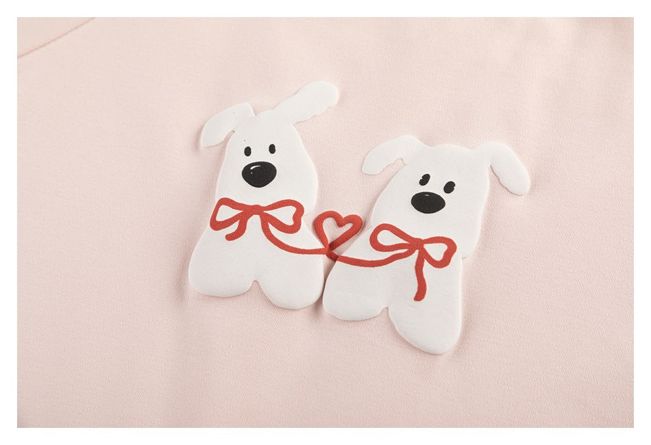 Close-up of two white dog illustrations with red bows on pale pink fabric.
