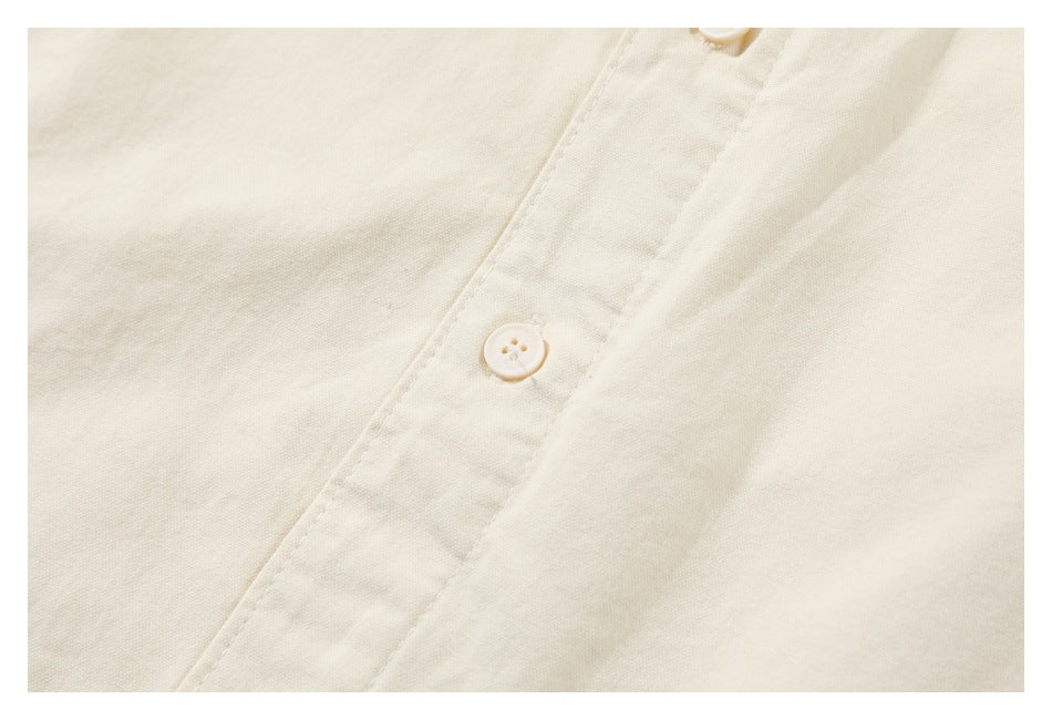 Close-up of a cream button and stitched placket on off-white fabric.
