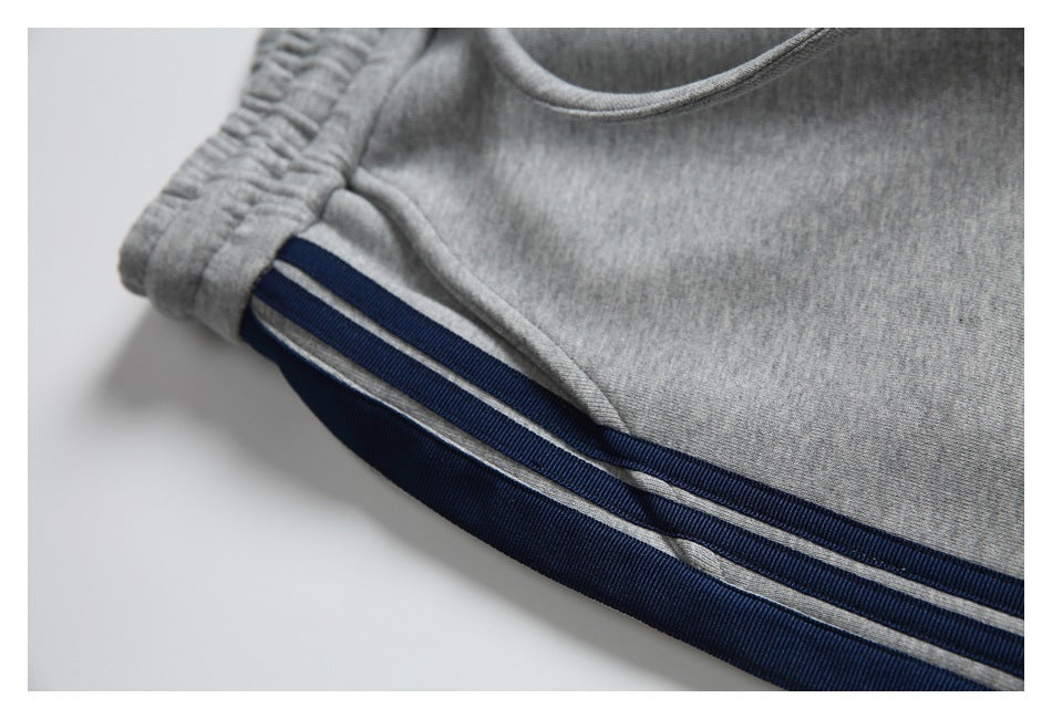 Close-up of gray sweatpants with navy side stripes and narrow light-colored accent stripes.