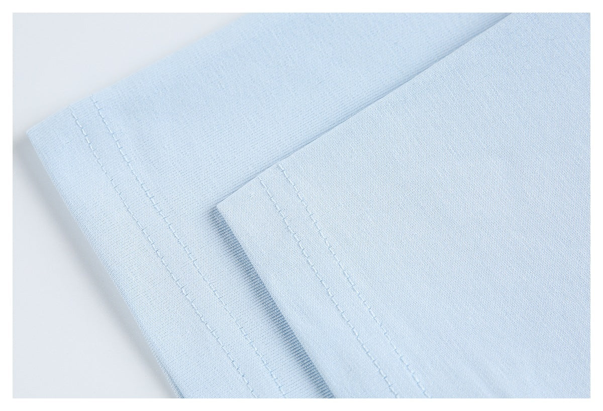 Close-up of two folded edges on light blue fabric, each with parallel stitching.