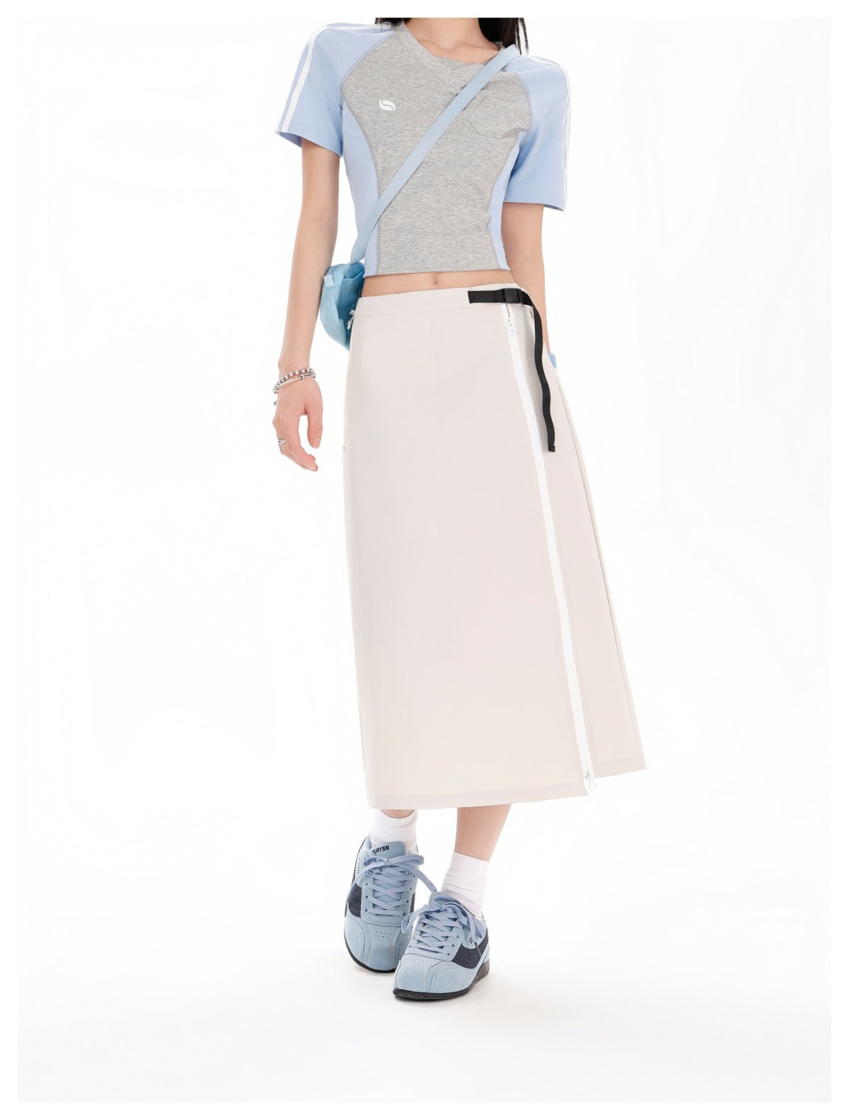 Model wearing an ivory midi skirt with a long white side zipper and black belt detail, paired with a gray and blue cropped