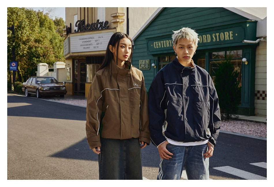 Two models pose in brown and navy high-collar jackets with white piping and front pockets.