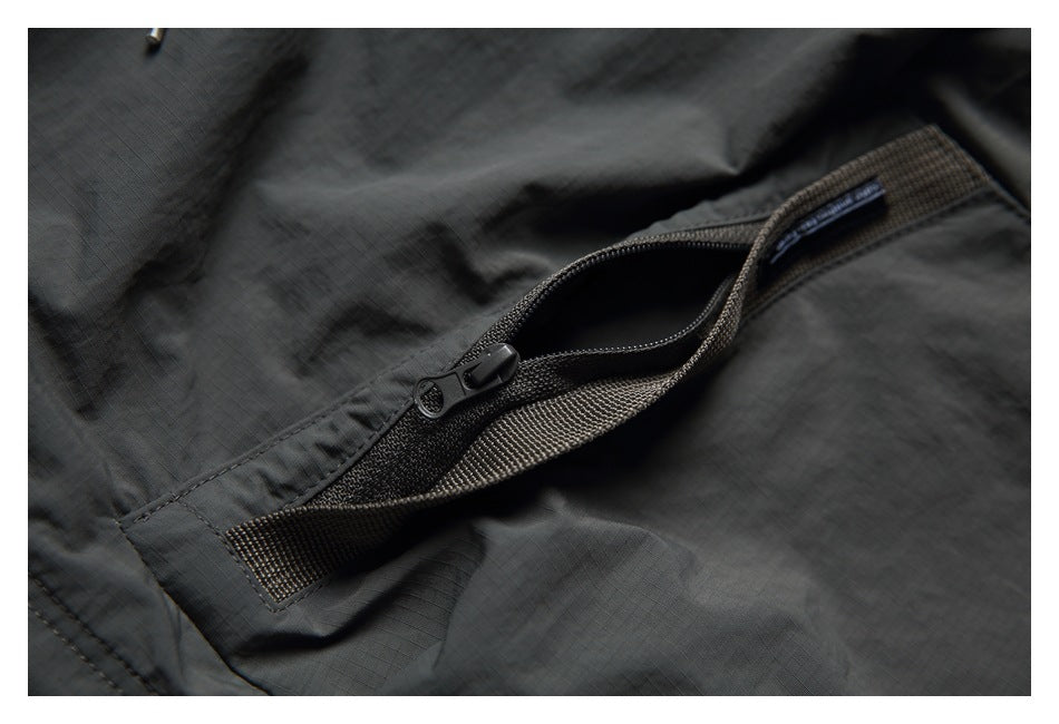 Close-up of a dark charcoal garment's open zipper pocket and woven trim.