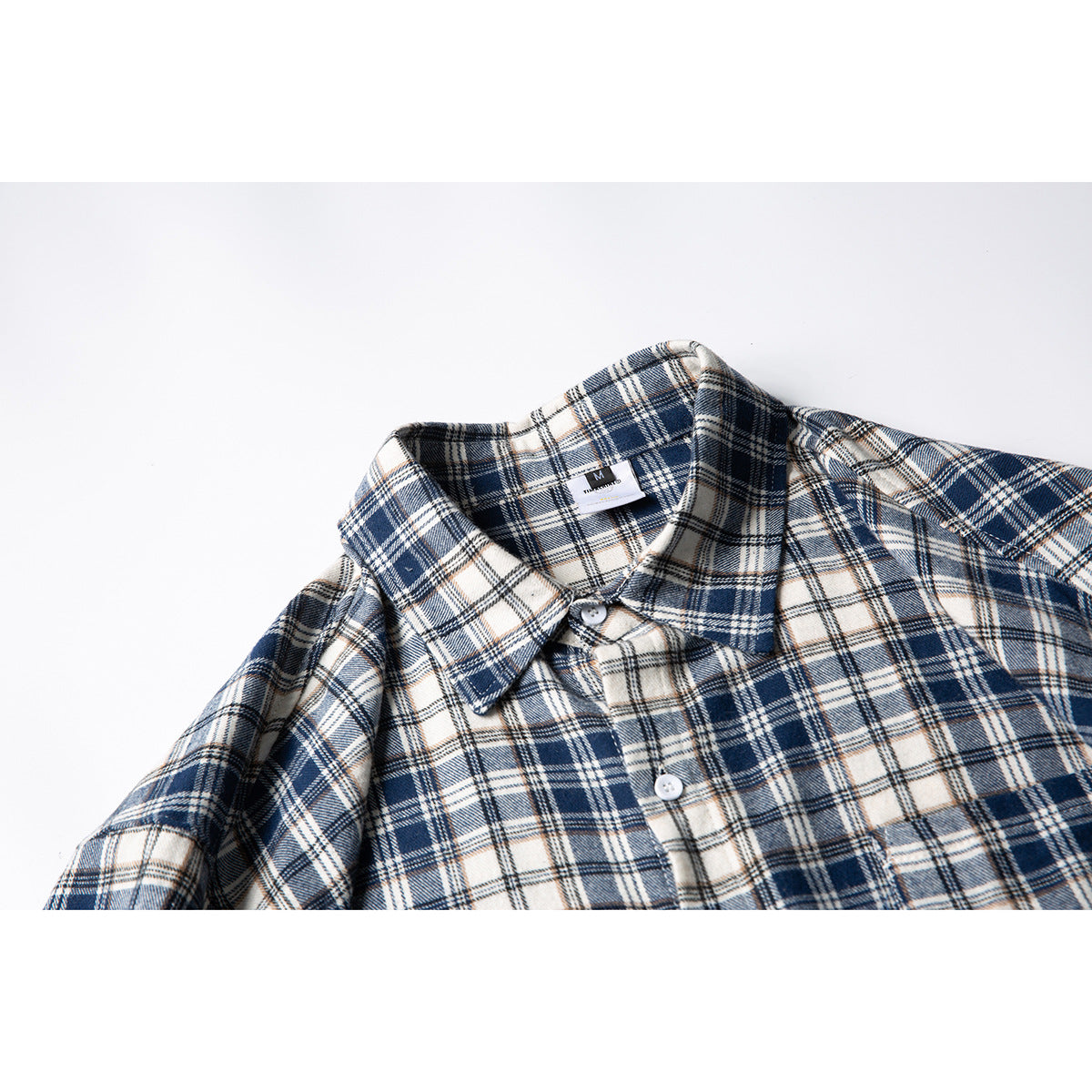 Close-up of a navy, cream, and tan plaid shirt collar with white buttons and a small neck label.
