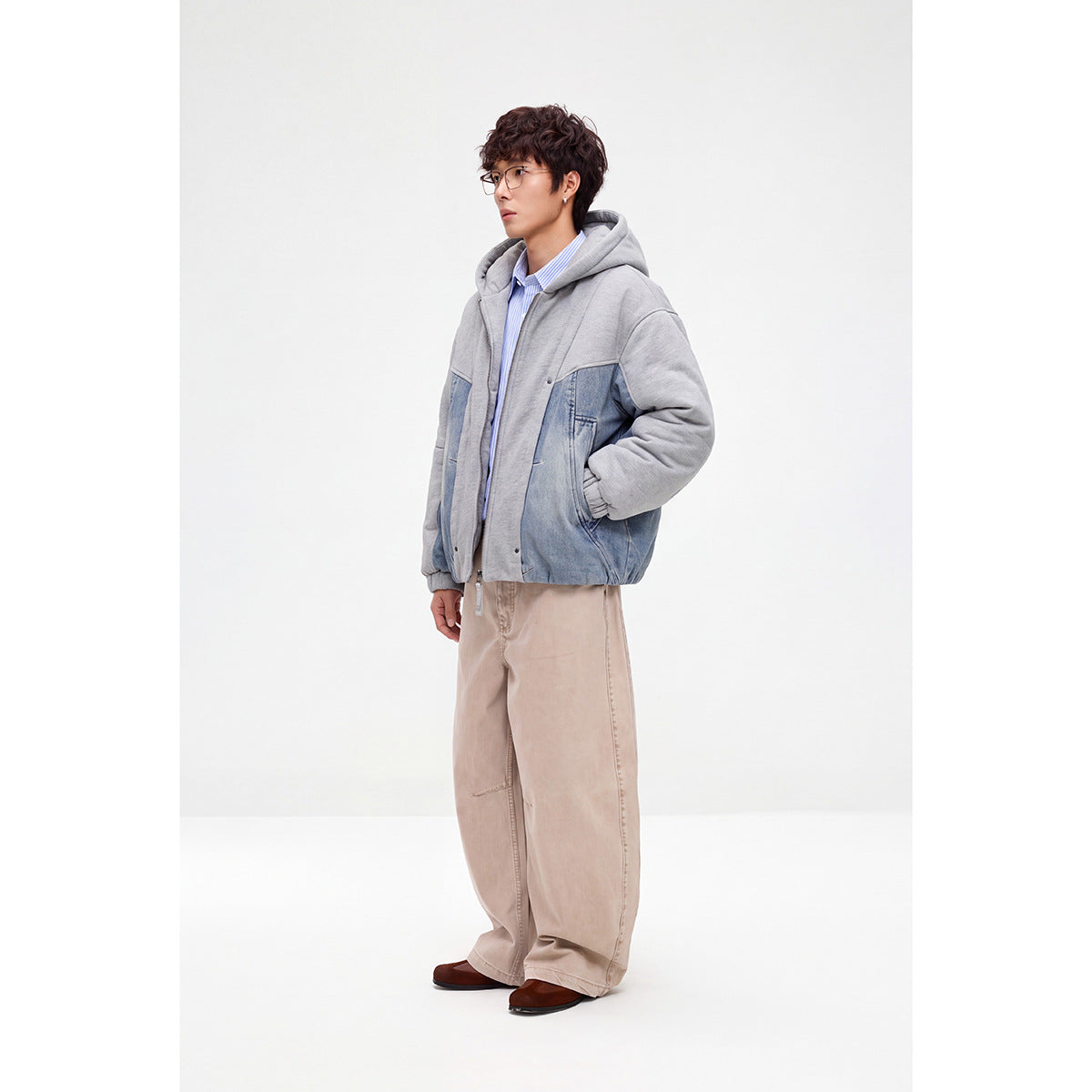 Model wearing a gray hooded zip jacket with blue denim panels, shown at a three-quarter angle.