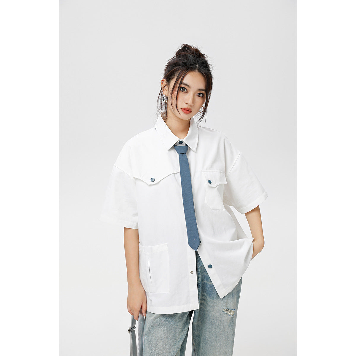Model wearing white short-sleeve shirt with blue necktie and chest pockets, with light-wash ripped jeans