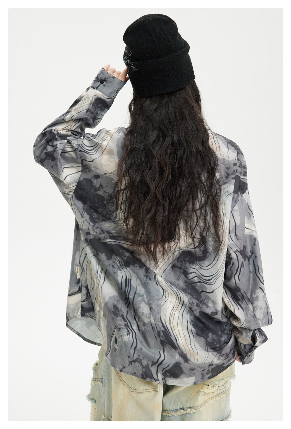 Rear view of a model wearing a loose gray and ivory abstract-print shirt with dark wavy lines.