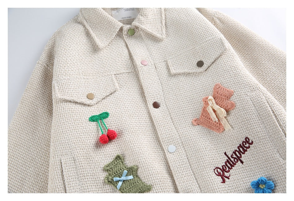 Close-up of the jacket front with flap pockets, multicolor buttons, cherry and flower appliqués, and embroidery.