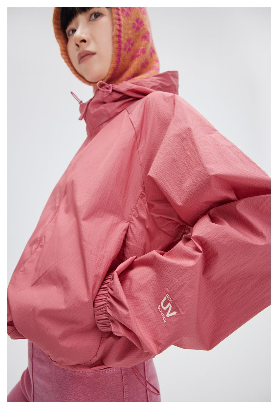 Close-up of a rose-pink hooded jacket showing its textured fabric, hood drawcord, sleeve cuff, and small sleeve graphic.
