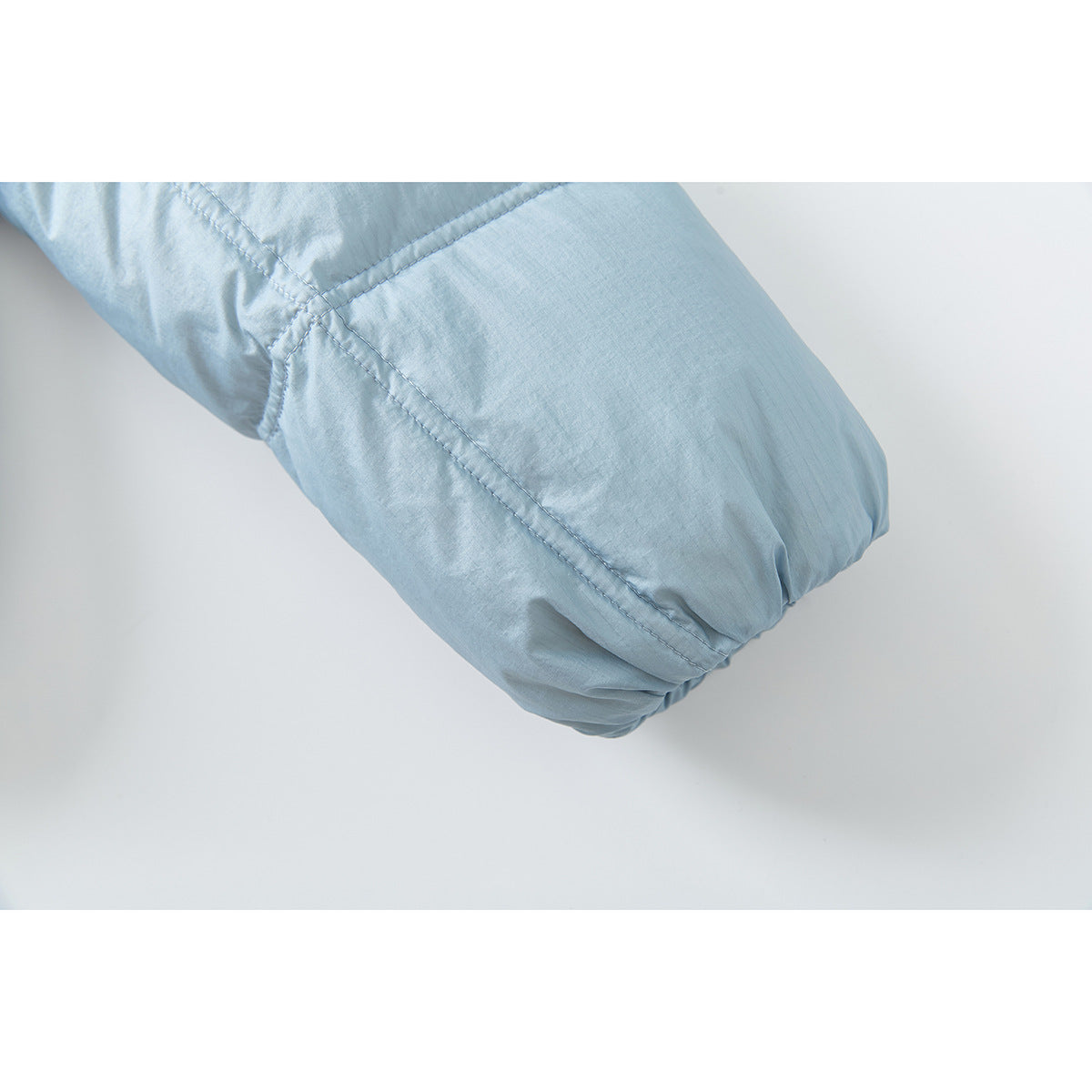 Close-up of the gathered cuff and stitched seams on a pale blue puffer jacket sleeve.